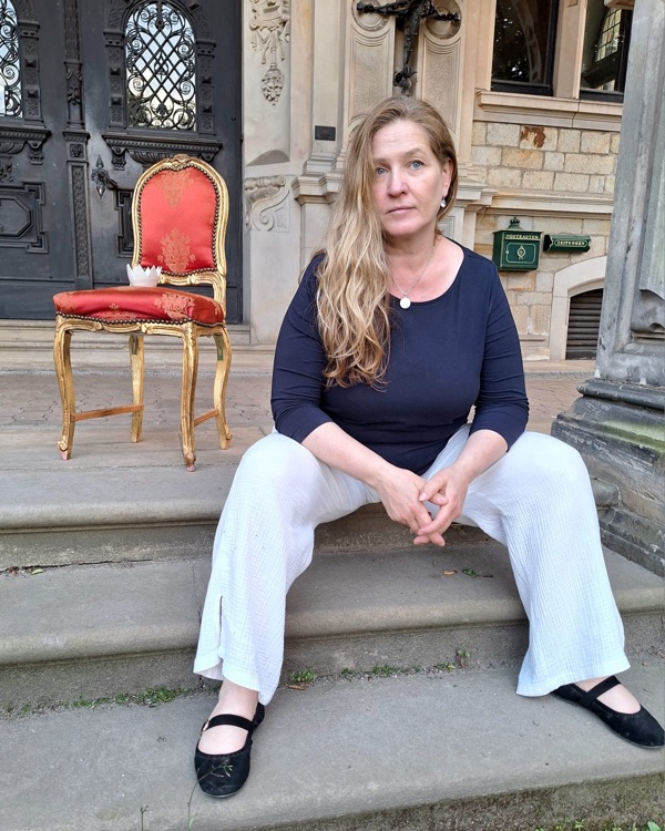 Steffi sitzt auf den Stufen eines alten Hauses, neben ihr ein roter Samtstuhl