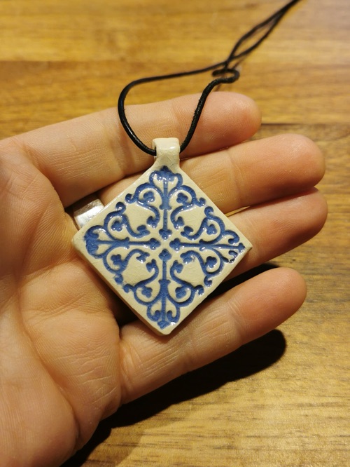 Keramik-Anhänger mit blauem Kachelmuster an einer Schnur auf einer Hand