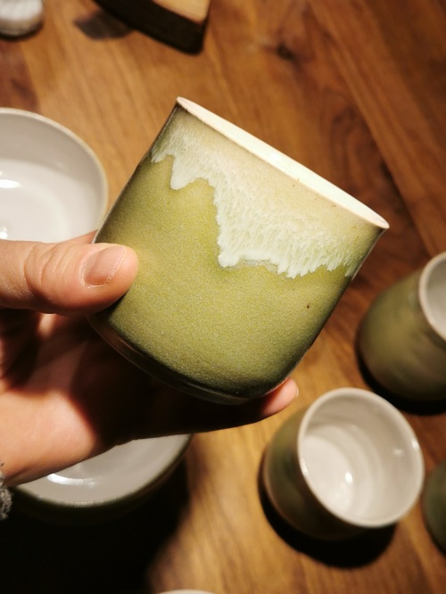 Becher mit grüner Glasur und weißer Laufglasur in einer Hand