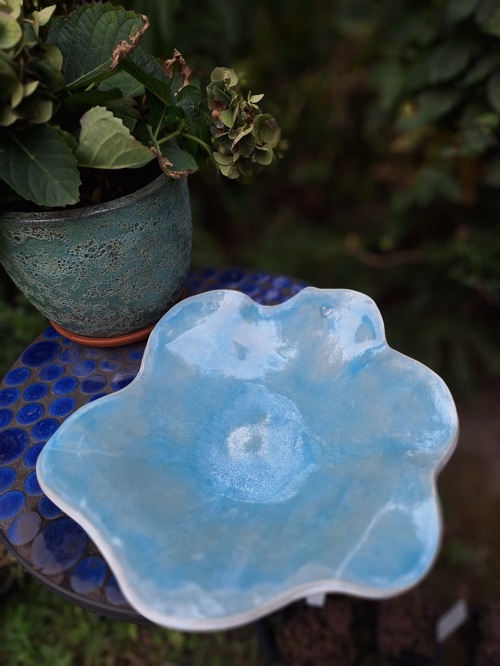 Hellblau glasierte Schale in Blütenform auf einem Mosaiktisch