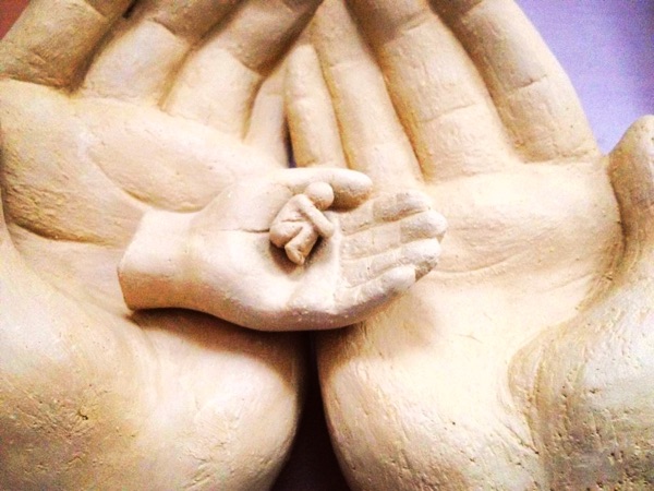 Skulptur aus Ton: zwei große Hände umschließen zwei kleine Hände