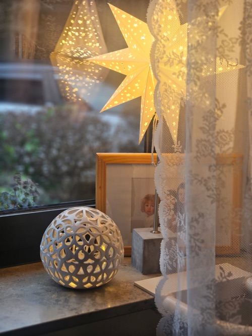 Von innen beleuchtete Lichtkugel am Fenster, daneben Papiersterne