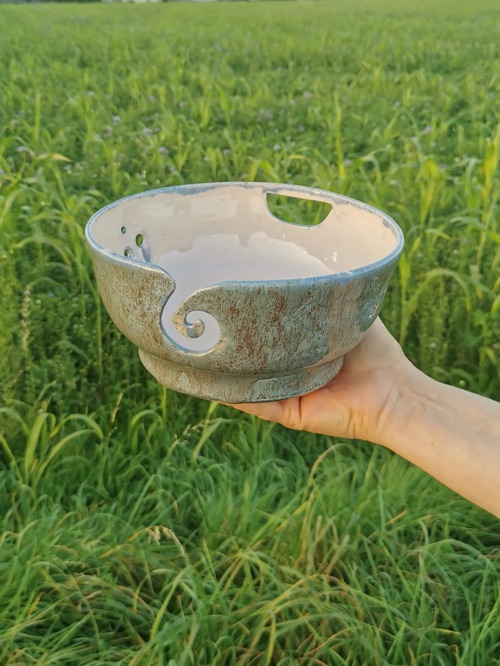 Hellblau glasierte Schale mit Spiralschlitz, gehalten über einem Feld