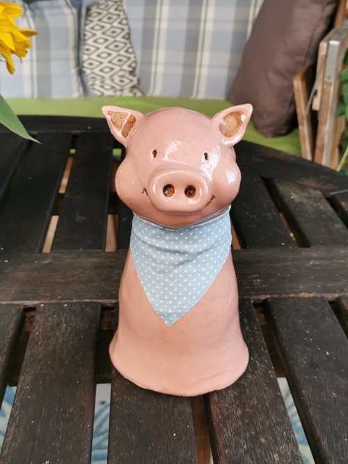 Rosa Schweinchen-Figur mit blauem Halstuch auf einer Gartenbank